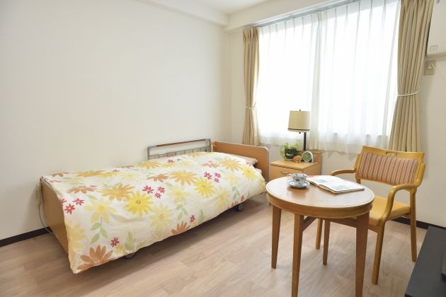 居室内はフローリングで窓があり、エアコンが備わっている。介護用のベッドの側にはサイドテーブルが置かれている。