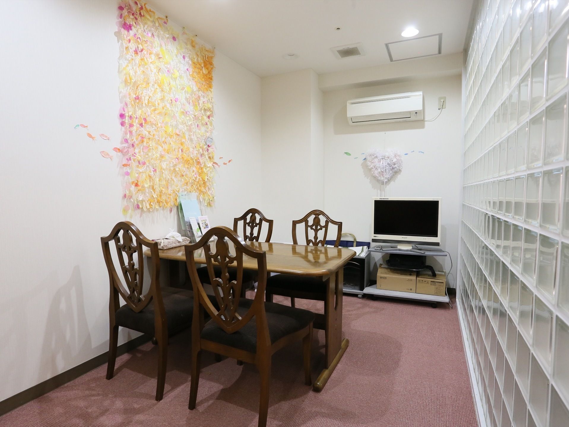 テーブルには椅子が４脚用意されている。テレビとエアコンが完備されており、淡い色合いの魚の壁掛けが飾られている。