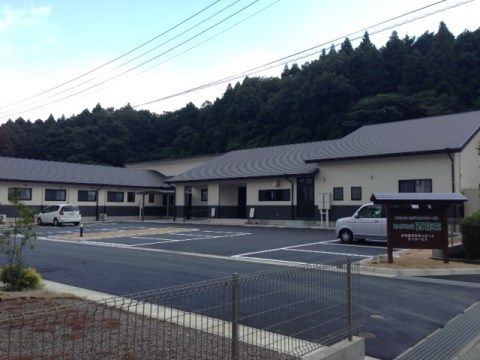 駐車場を囲むように建つ、落ち着いた外壁の平屋の建物
