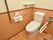 洋式トイレで、壁や便座の横に手すりが設置されている。真ん中が青色の丸いボタンは緊急時の呼び出しボタンである。