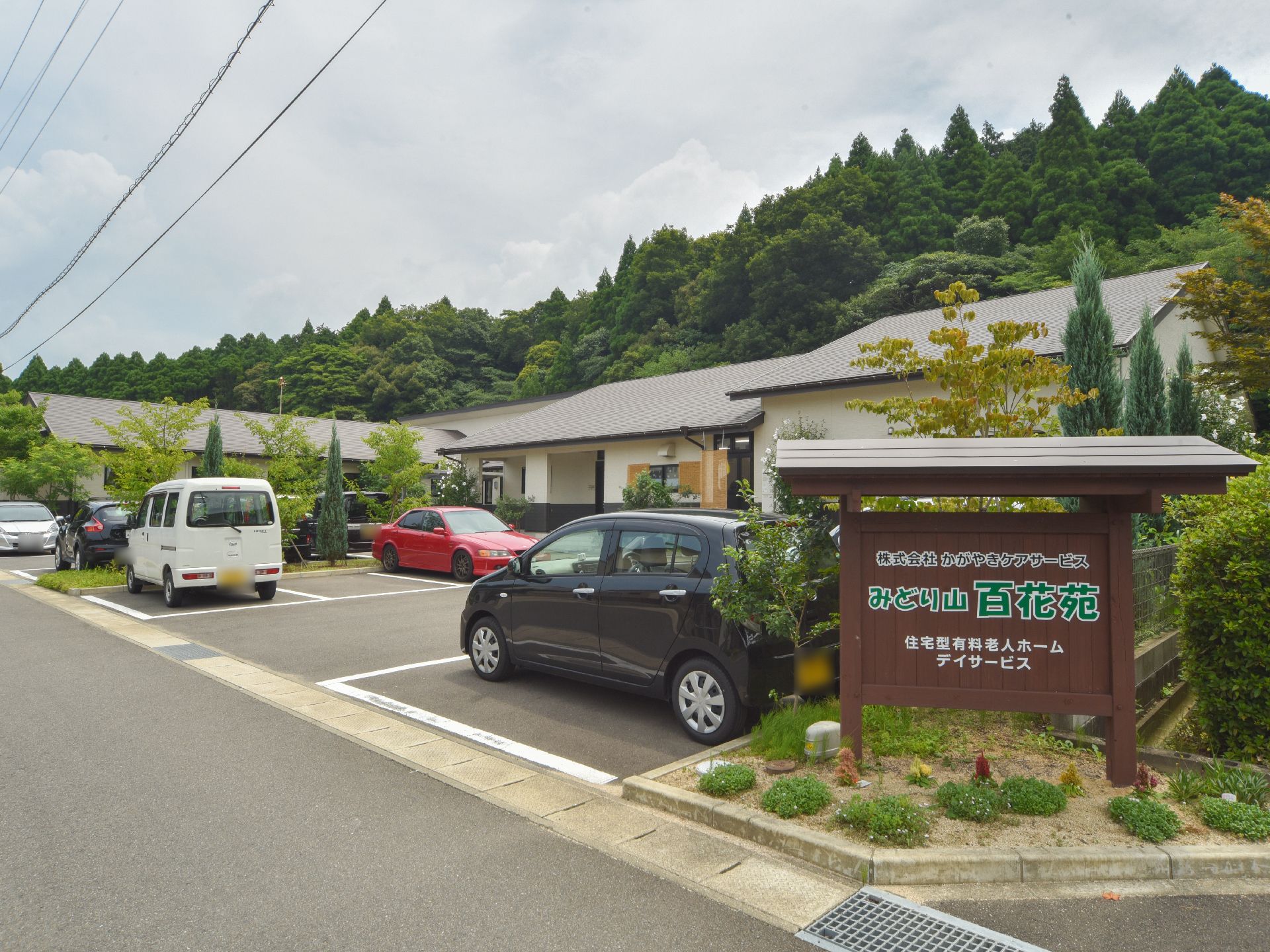 敷地の角に屋根のついた木の看板が立っており、施設名が書かれている。看板の下のは草花が植えられている。