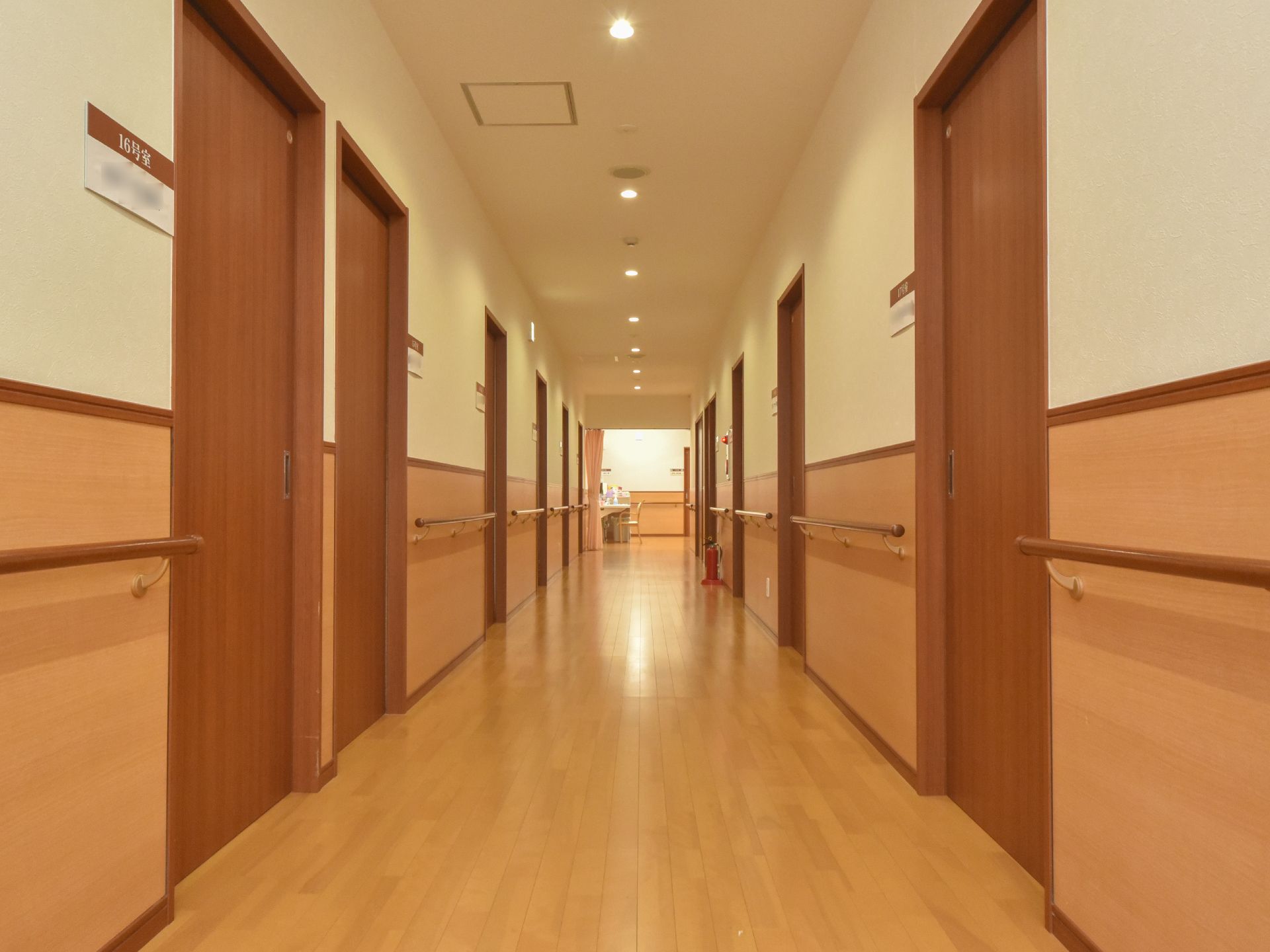 廊下の両脇に居室のドアが並んでおり、壁に手摺りが設置されている。ドアの横に表札があり、部屋番号と入居者の名前が書かれている。