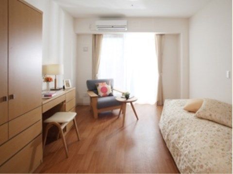 居室は奥行きのある設計で、床はフローリングとなっている。右側にはベッド、左側にはタンスや机が配置されている。