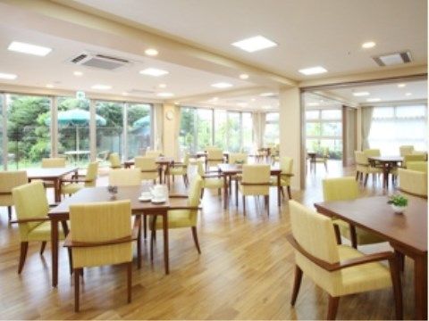 ダイニングルームには、黄緑色の椅子と四角いテーブルがたくさん用意されている。部屋の奥は、全面ガラス張りとなっている。