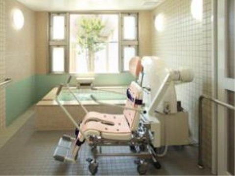 大きな窓があるタイル張りの明るい浴室に、座ったまま入浴できる車椅子がある。電動で浴室まで移動する機械がある。