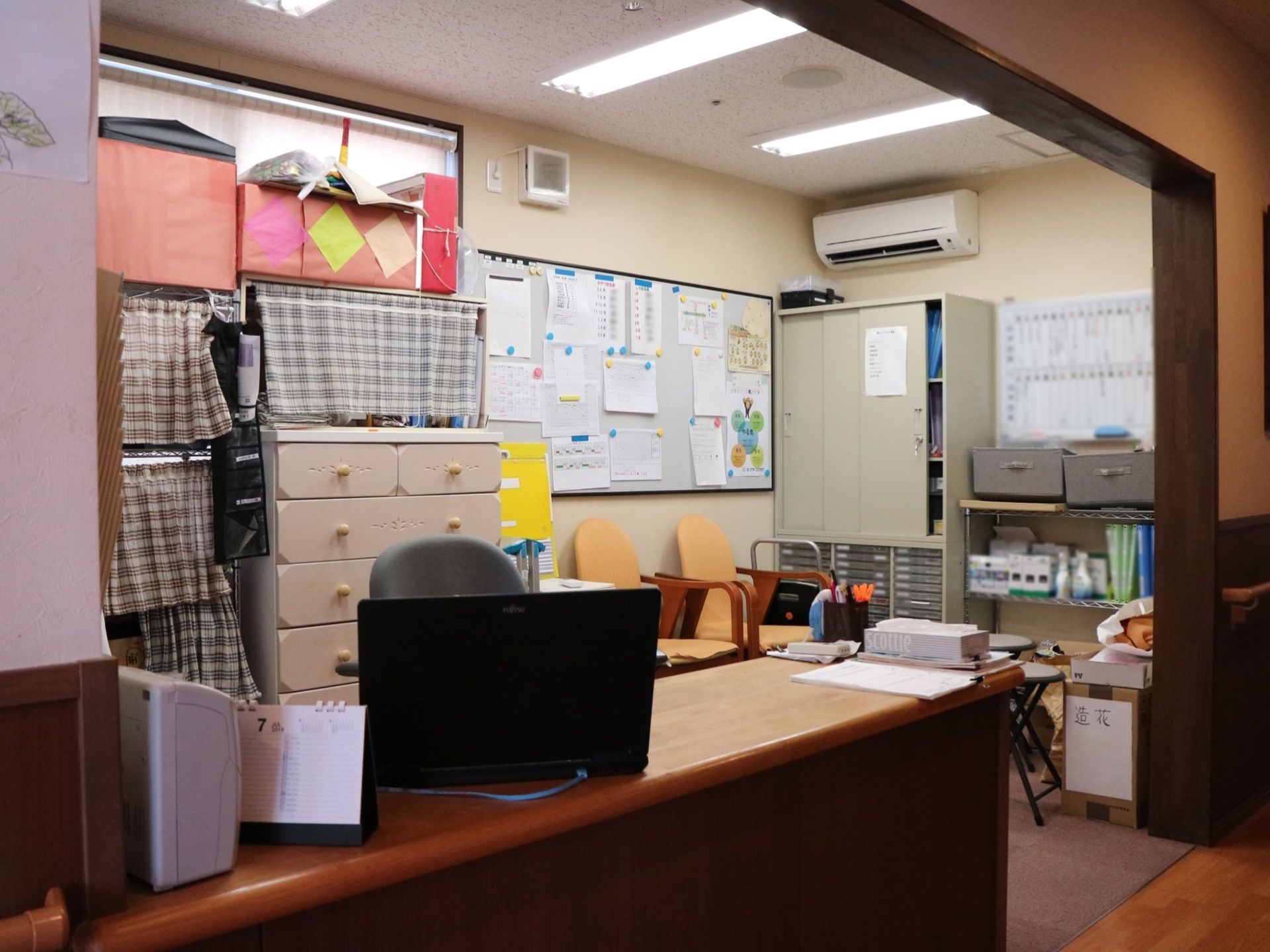 仕切りのない部屋に横長の低いカウンターが置かれている。奥にはアルミ製の棚や小さなタンス、ホワイトボードなどがある。