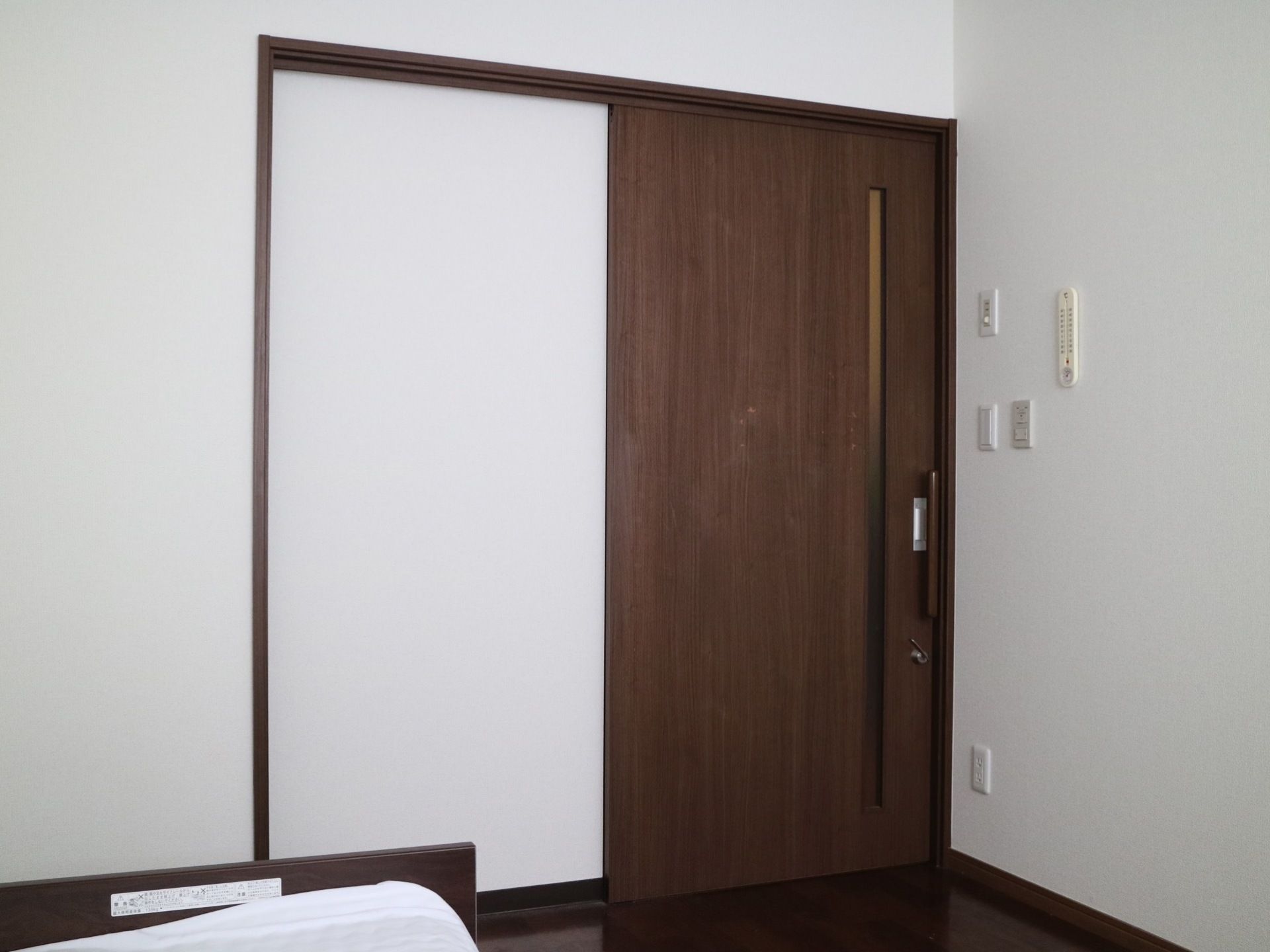 居室のドアは引き戸式になっている。ドアに縦長の手すりが付いている。部屋の中の壁には温度計が取り付けてある。