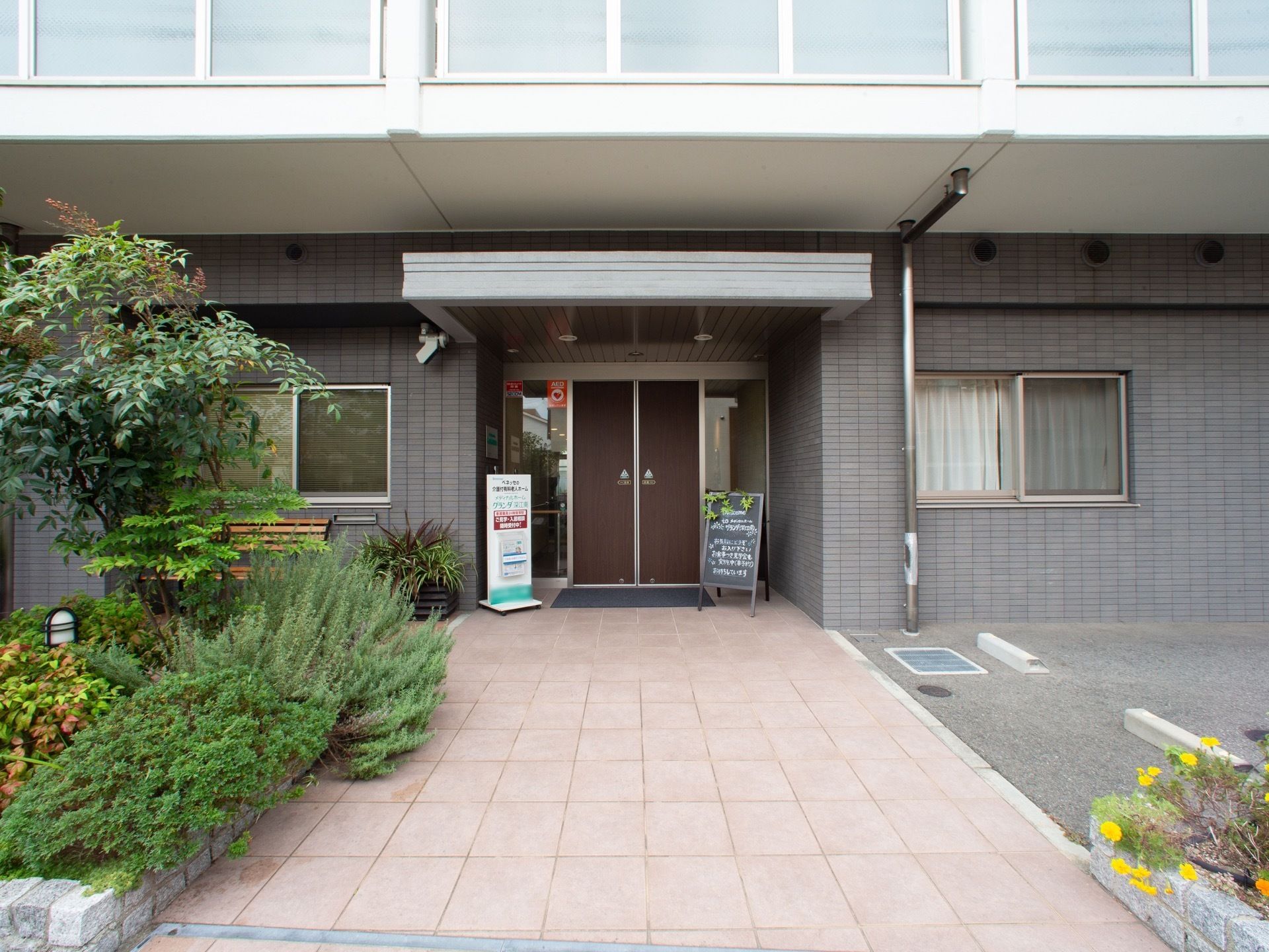 緑豊かな花壇やベンチ、自動ドアが配置されたエントランス