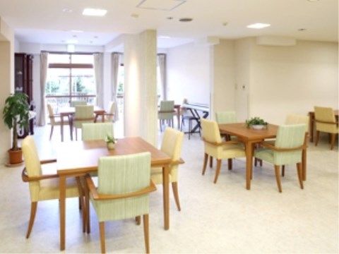 壁と床が白く窓がある明るい室内に、座面が薄い緑色で肘付き椅子のダイニングセットが間を空けて並んでいる。