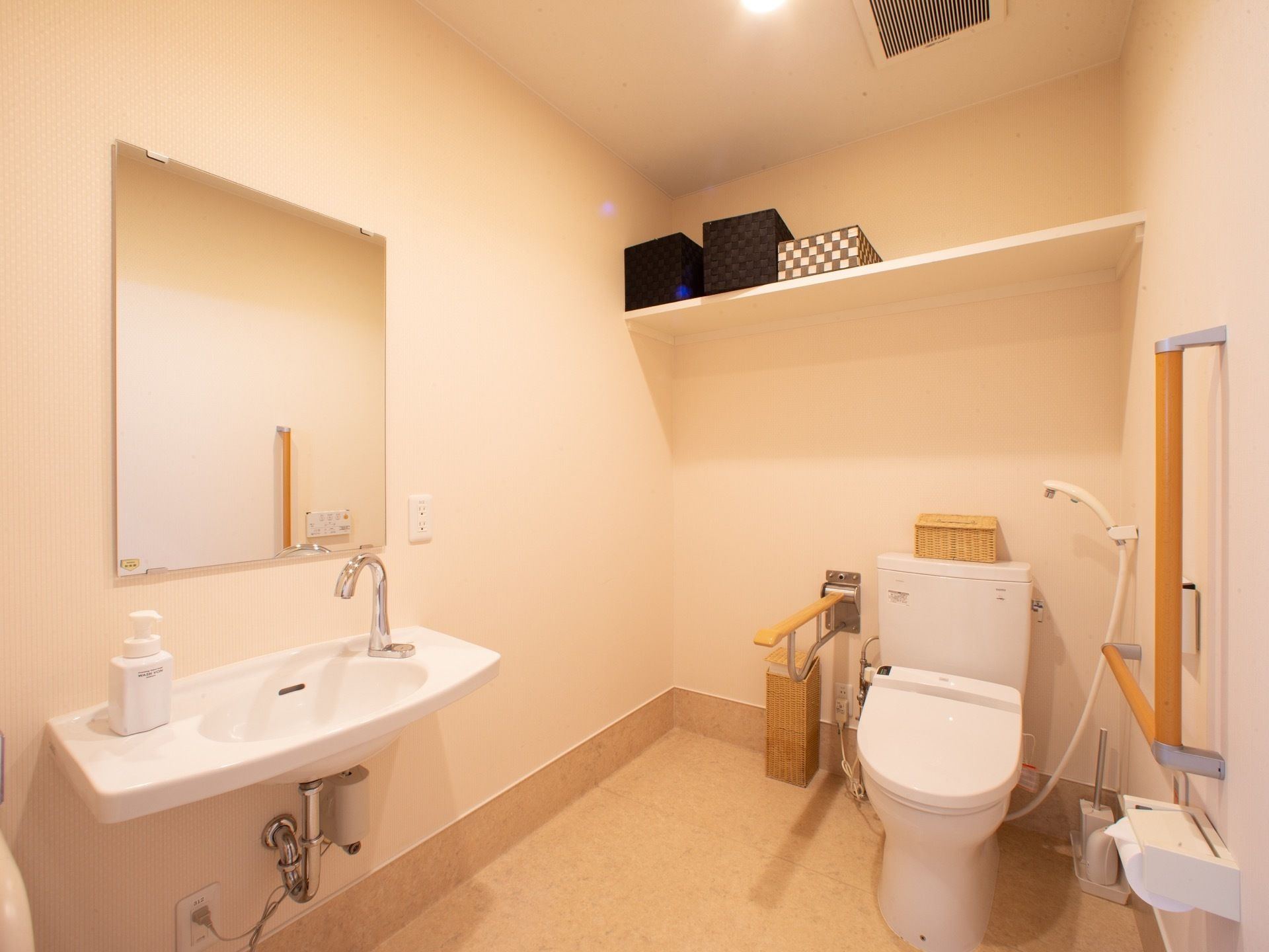 手すりとトイレシャワーが備え付けられており、鏡のついた洗面台が併設されているトイレ