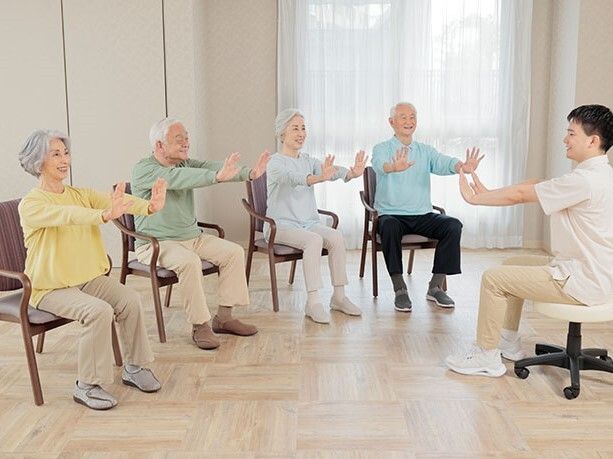 歩行器を押しながら歩く高齢男性の背に手を当ててサポートする男性
