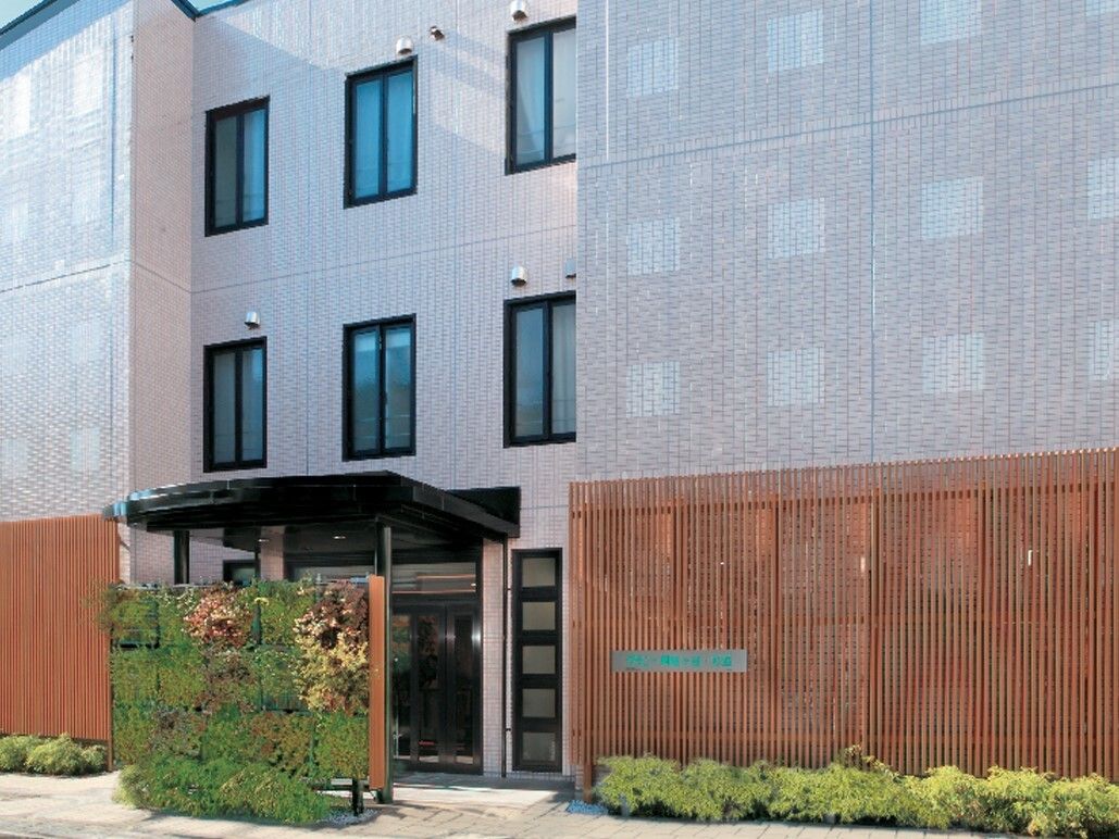 建物の周りや正面の植栽が印象的な３階建ての建物。１階部分には木製の柵が設置され、程よく外からの視線を遮っている。