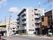 周辺を一般住宅街に囲まれた施設は5階建てであり、日当たりが良く道路に面していて数台の車が停まっている。