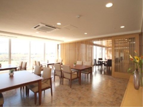 食堂には茶色いテーブル、ベージュ色の椅子が並んでおり、扉でスペースが2つに分けられている。棚には花が飾られている。