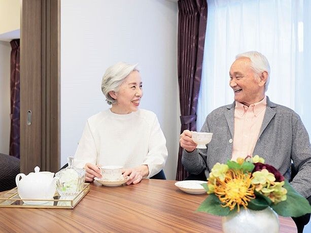 男性の誘導を受けながら、手すりを伝い廊下を歩く高齢男性