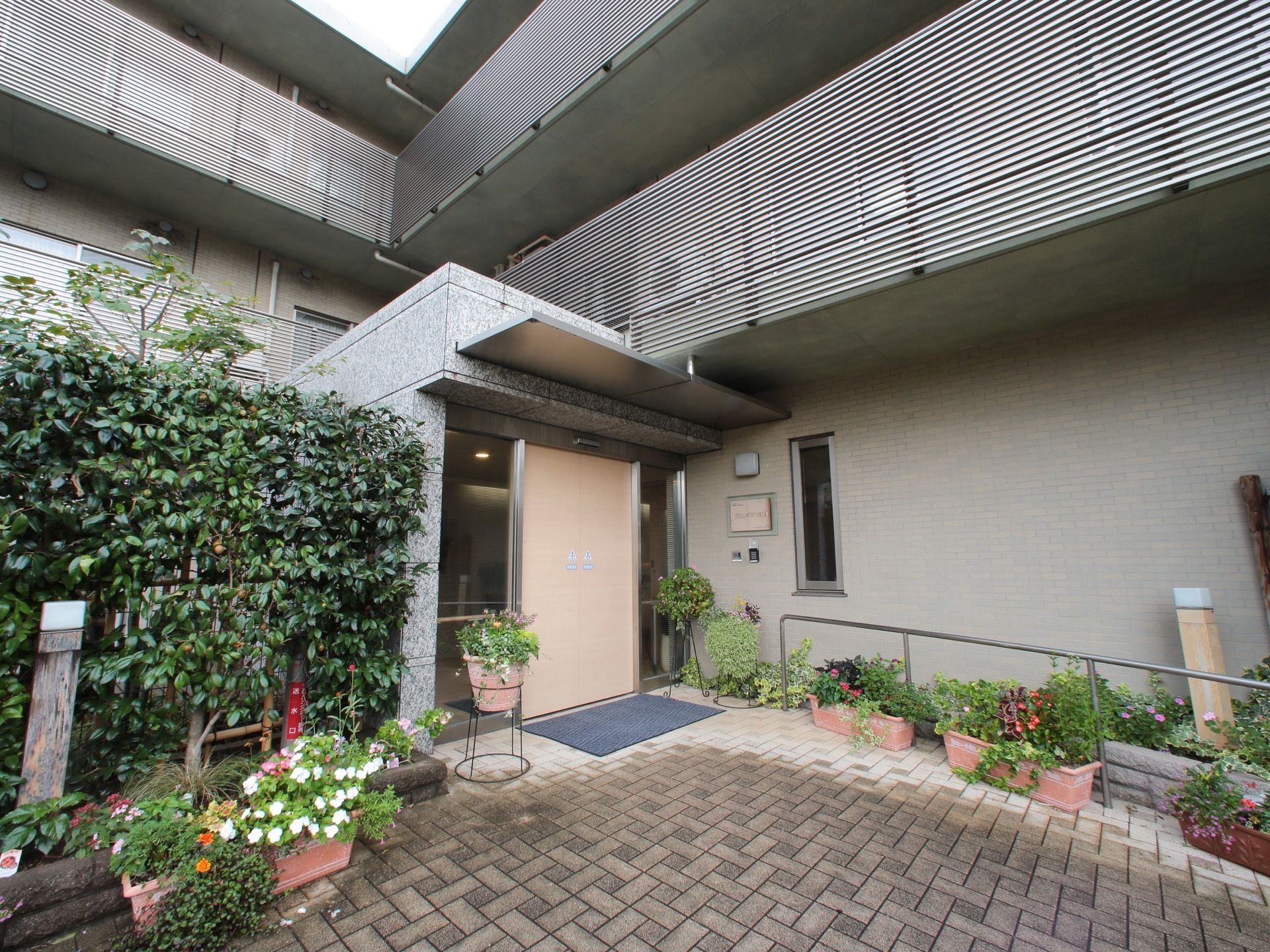 花壇や植木の置かれた自動ドアのあるエントランス入口