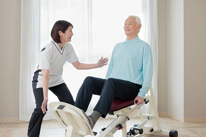 椅子に座り、男性スタッフに足の状態を確認してもらっている高齢女性