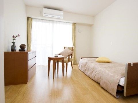 ベッドや机、椅子、タンスなどがすっきりと配置された居室である。窓からは自然光が差し込み、明るい雰囲気になっている。