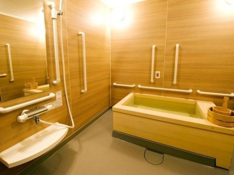 木目調の壁、檜の浴槽が和の雰囲気を醸し出す落ち着いた浴室になっている。スタッフが介護しやすいように浴槽の周りにスペースがある。