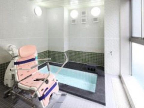 座って入浴できる設備が置かれている浴室。その正面には窓があり、白く光っている。壁の上部に丸い照明が３つ設置されている。