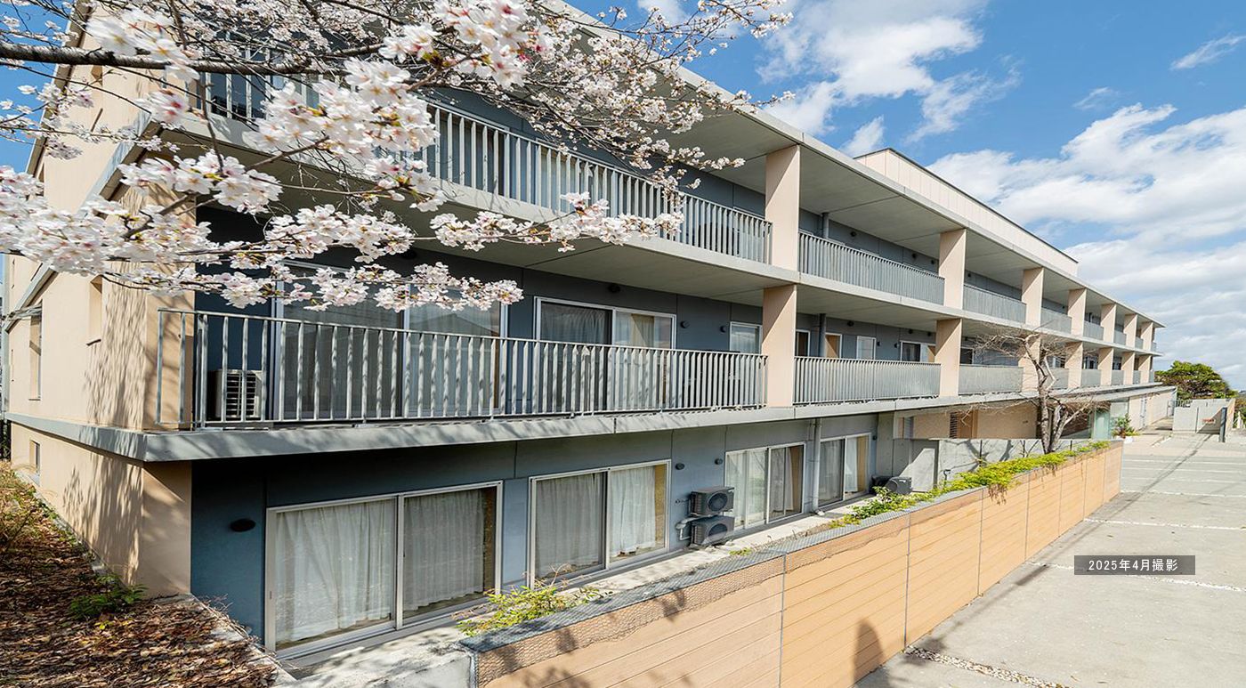 居室の窓周りの濃い青色を基調とした外壁が印象的な３階建ての施設