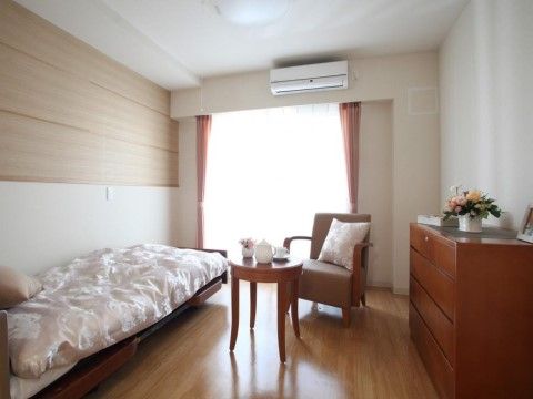 大きな掃き出し窓からやわらかな日差しが差し込む明るい居室である。木目のフローリングが温かみを感じさせる。