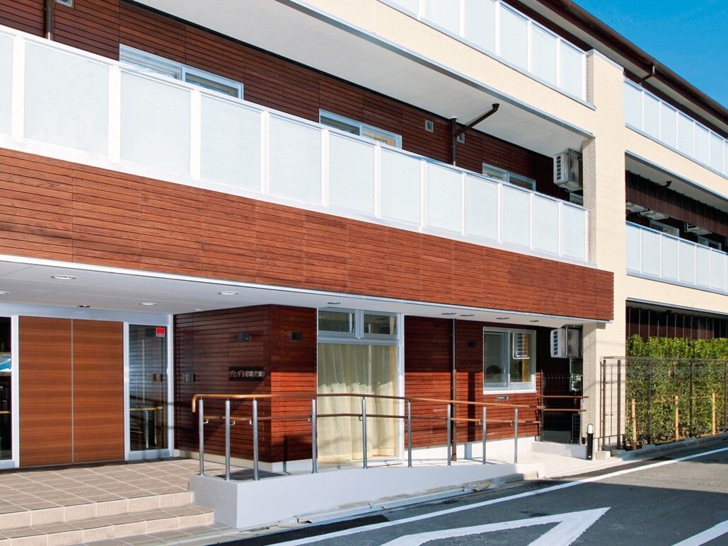 通りに面した３階建ての建物。入口へのアプローチは手すり付きの階段とスロープの両方が設置されているので安心である。