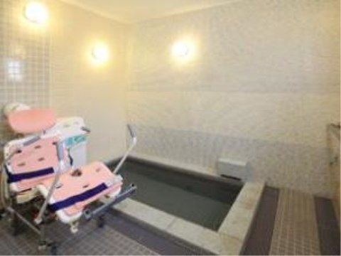 車椅子のご入居者様でも入浴できるリフト浴がある。白とグレーのタイルの壁の浴室である。照明も多くついており明るい。