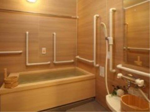 木目の壁が特徴的な木のぬくもりが感じられる浴室。壁には手すりがまんべんなく備え付けられており、木の桶が置かれている。