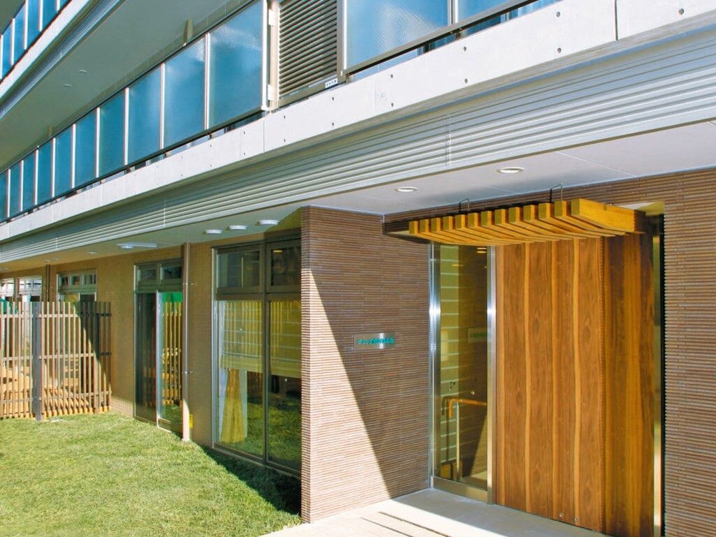 ３階建ての建物が見える。ベランダが写っている。玄関は小さな段差が２段設けられている。扉は木製である。