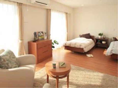 大きな掃き出し窓がある幅広い部屋には、奥の壁に頭を向け、窓と平行にベッドが２台並んでいる。手前には１人掛けのソファが２脚ある。