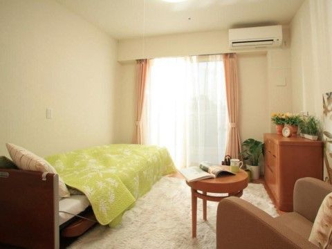 突き当りに掃き出し窓があり、上にはエアコンが設置してある。窓に向かって左側にはベッドがあり、向いの壁には整理ダンスが置かれている。