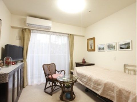居室の壁際にベッドが置かれている。壁にはたくさんの写真が飾られている。天井近くにエアコンが完備されている。