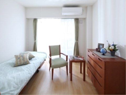 ゆとりあるスペースを確保した居室には、大きな窓やエアコンが完備されている。薄いモスグリーンと赤い茶系が配色でまとめられている。