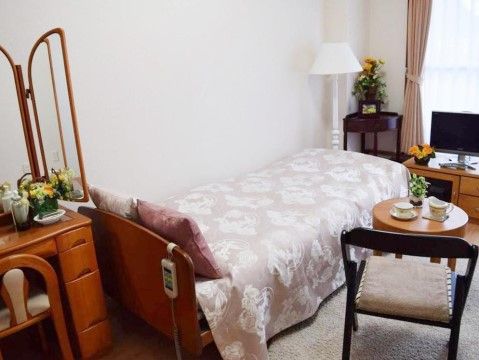 ベッドや電気スタンド、鏡台、コーヒーテーブルと椅子、テレビ台などの置かれた部屋である。居心地よく整えられている。