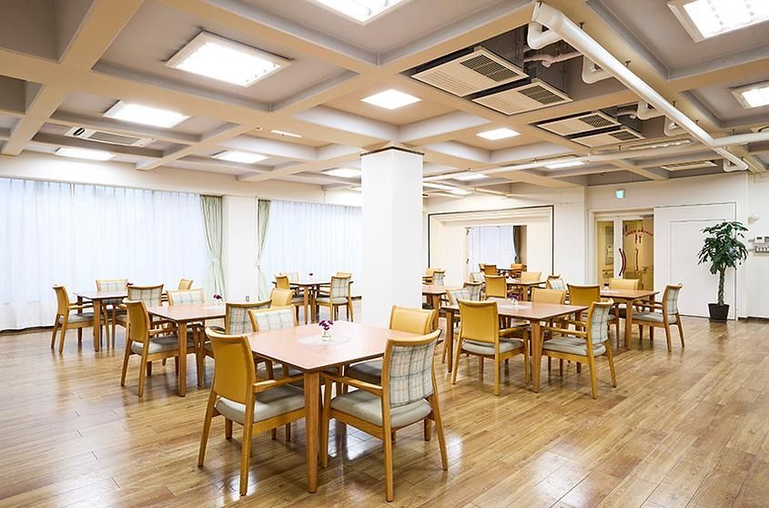 板張りの床に格子状の天井というデザインの空間に、テーブルと２色の椅子が複数置かれている食堂