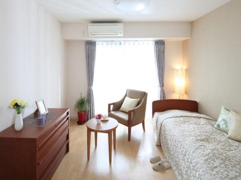 天井の近くまである大きな掃き出し窓から、外光が入る明るい部屋。木製のチェストに、一人用のテーブルセットが置かれている。