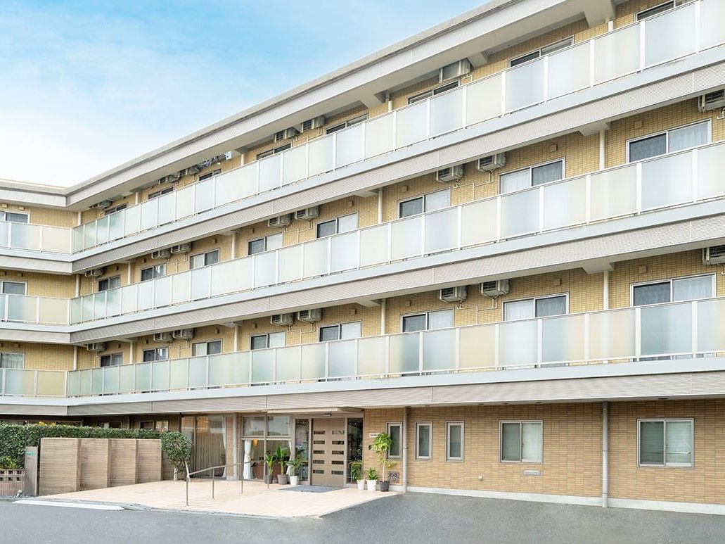 ベージュを基調とした4階建ての建物。２階以上の居室には日当たりを妨げない柵付きのベランダがあるので安心である。