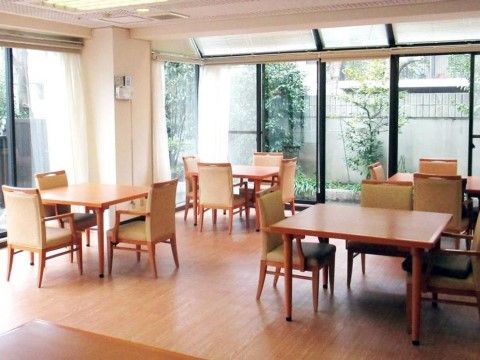 木目調のダイニングテーブルがいくつも置いてある。窓が大きく明るい室内である。外には庭の植木が見える。