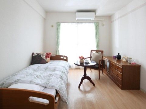 居室にベッドを置き、小さな丸テーブルや椅子を配置している。収納用にキャビネットを入れて、快適に過ごせる居室を作っている。