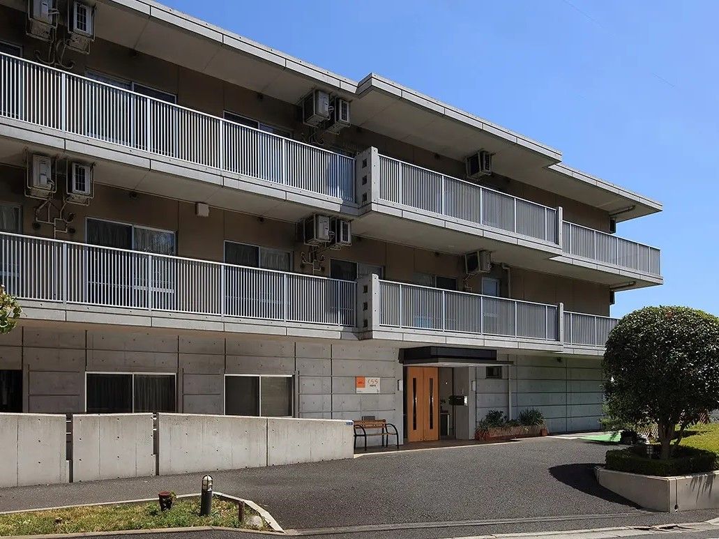 グレーの石貼り風の外壁が印象的な鉄筋コンクリート造３階建ての建物。車が乗り入れしやすい、広い入り口になっている。