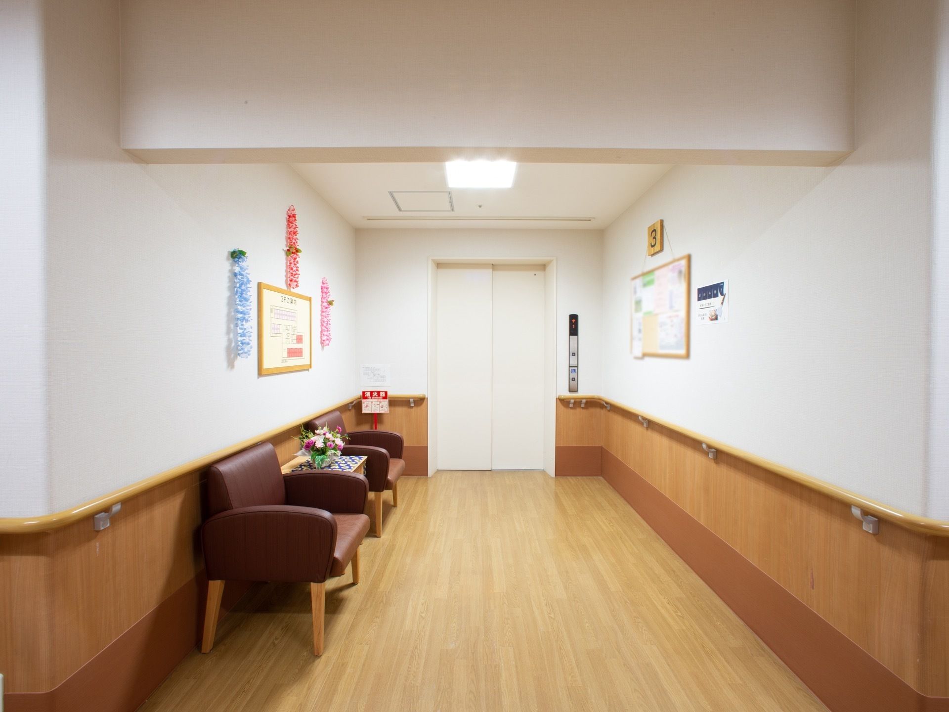 明るい照明と、手すりが配置されたエレベーターホール