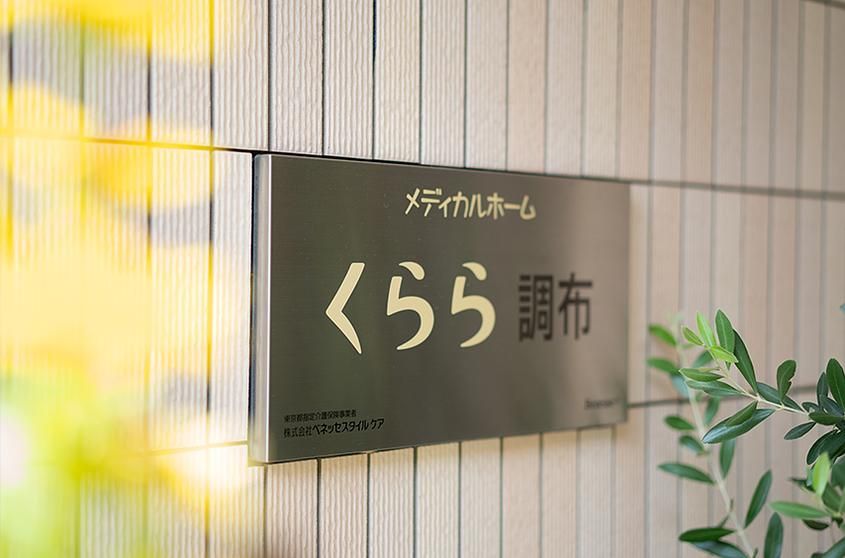 フローリングの部屋に電動ベッド、エアコン、テーブルセットがある。ベランダに続く大きな窓があり、明るい部屋である。