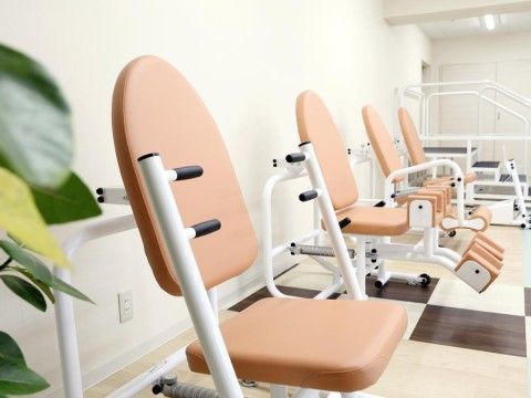 レッグエクステンションやヒップアブダクションなど種類の違うリハビリ器具が壁沿いに置かれている。壁にはコンセントがある。