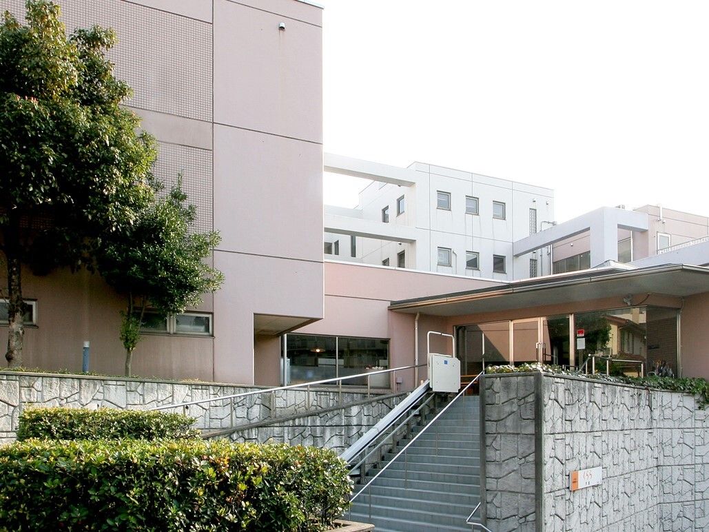 白を基調とした落ち着いた色合いの大きなグループホームである。施設目の前には、銀色の手すりが設置された階段がある。