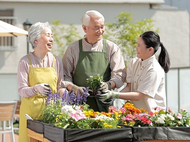 笑顔の男性スタッフの近くで草花の手入れをしている男性入居者様