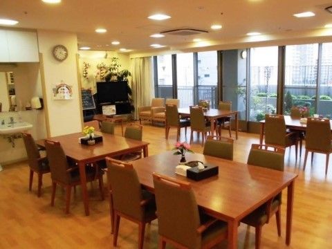 ゆったりとした広さのリビングルームには、４人掛けテーブルが多数並べられている。部屋の隅には、大きなテレビが設置されている。