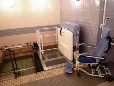 浴室は広く、入浴用の青色の車椅子が置かれている。大きな浴槽には、車椅子をのせるための介護用機器が設置されている。