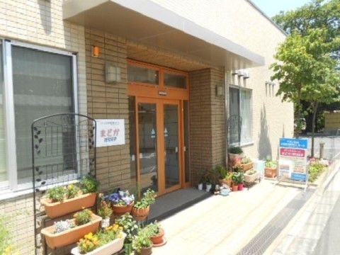 歩道から一段上がると玄関になっている。扉はガラスの自動ドアで、周囲はベージュのタイル張り、両側には鉢植えが並んでいる。