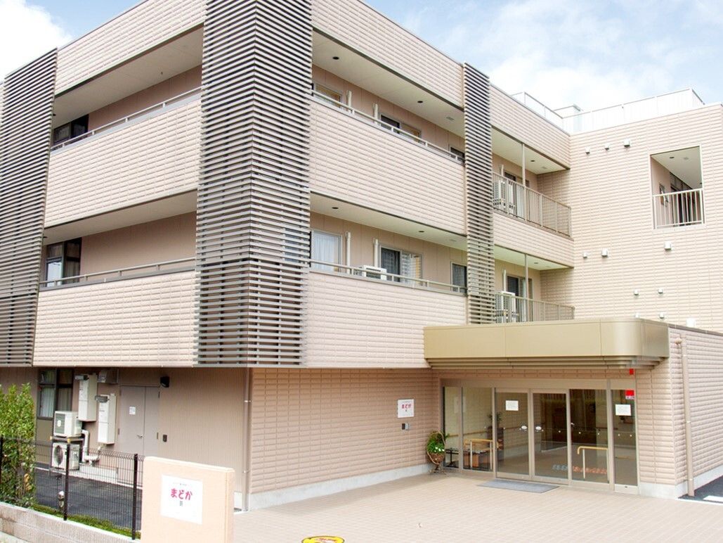 白とグレーのタイルの外壁に、玄関ひさしの部分が濃いベージュになっている3階建ての建物